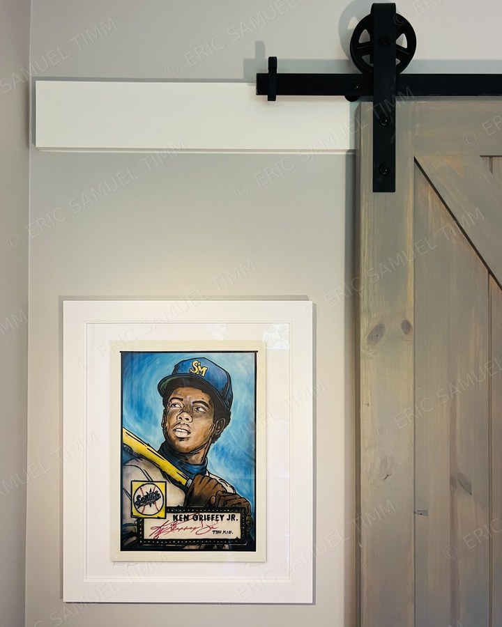 Framed Ken Griffey Jr. print in a white frame on a grey wall beside a sliding barn door